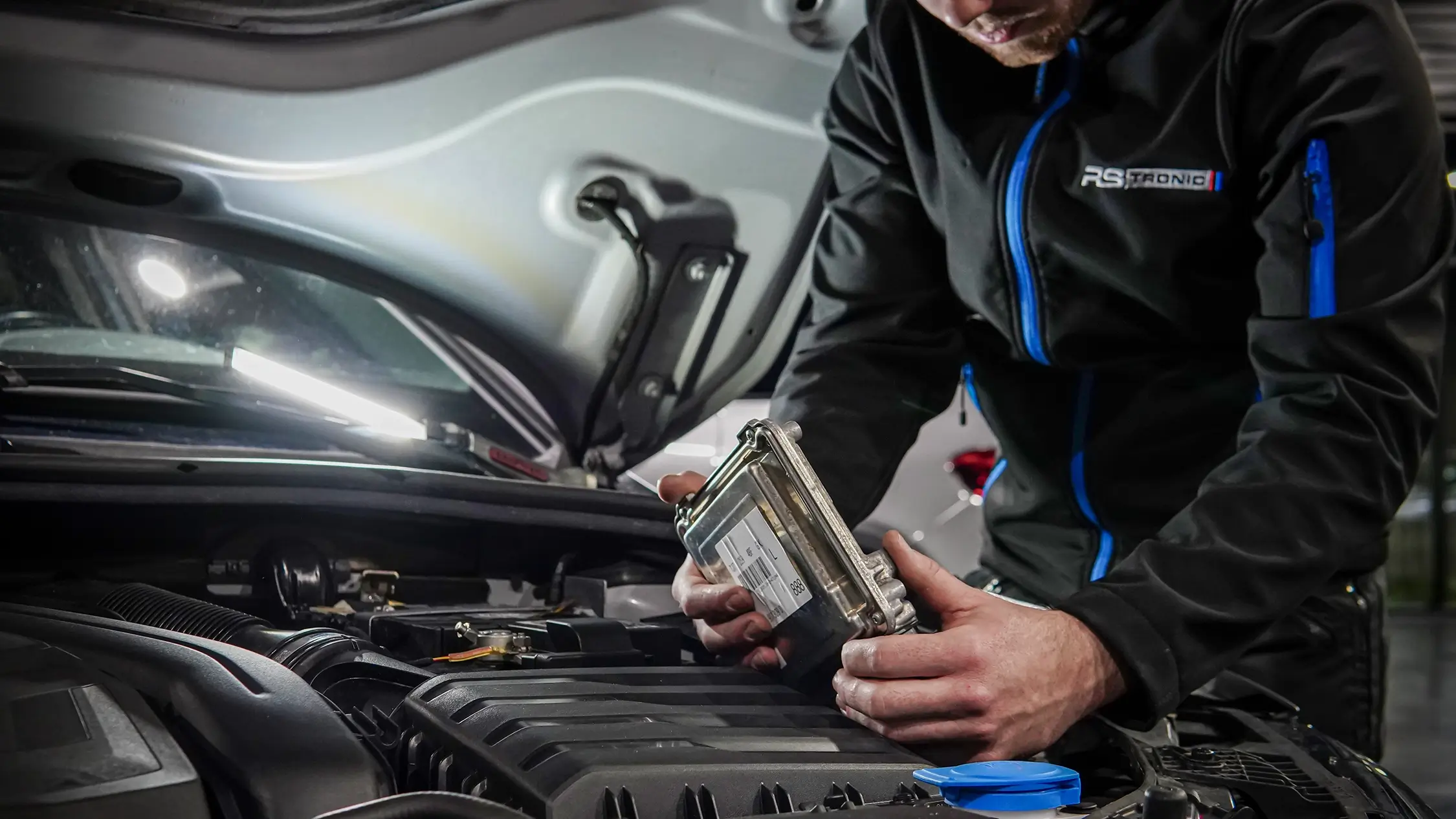 Technicien RS Tronic tenant un calculateur moteur au-dessus du compartiment moteur